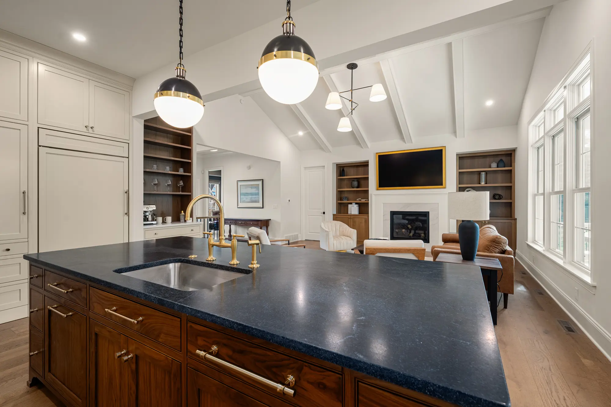 Kitchen in The Cabot Ridge with a dark-topped wood island, brass fixtures and globe pendants, open to the great room